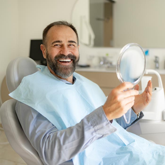 man looking at new smile in mirror in dentists office